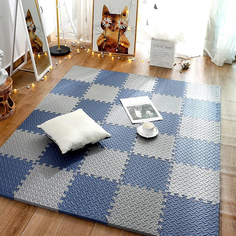 Checkered blue and gray foam puzzle mat on a wooden floor with a pillow and small table.