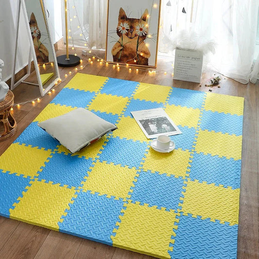 Yellow and blue interlocking foam mats on a wooden floor with a pillow and cup.